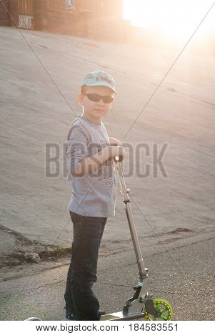 Little Boy In Sunglasses And A Cap Riding A Scooter,