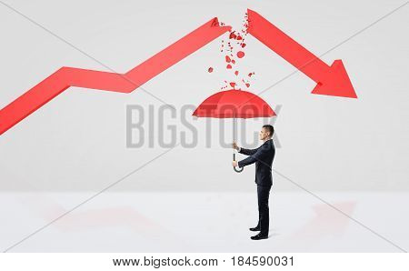 A tiny businessman hiding under a red umbrella from the rubble of a broken red statistic arrow. Business result. Success and failure. Surviving bankruptcy.