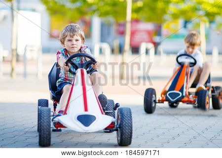 Two active little kid boys driving pedal race car in summer garden, outdoors. Children, best friends racing with fast speed and having fun. Twins making competition