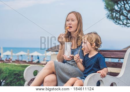 Mom And Son Eat Fried Sweet Potatoes In The Park. Junk Food Concept
