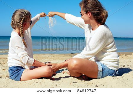Daughter and her mom playing with sand on the beach