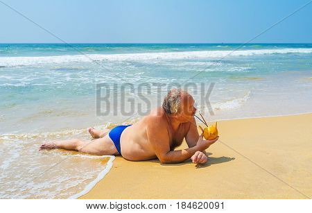 The tourist is sunbathing lying on the ocean's shore and enjoys the cocktail in coconut Boosa Sri Lanka.