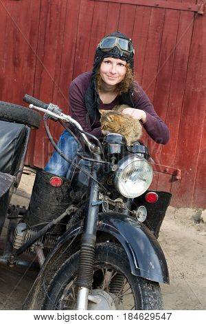 Photo of girl on vintage motorbike in pilot cap with cat