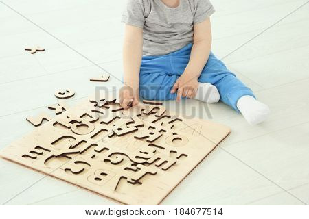 Cute little child playing with letters while sitting on floor at home