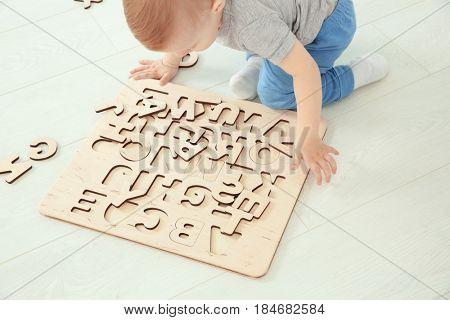 Cute little child playing with letters while sitting on floor at home