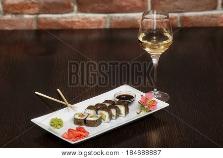 Sushi rolls with salmon and nori on white plate and glass of wine