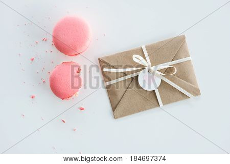 Top View Of Decorative Kraft Envelope With Bow And Pink Macarons Isolated On White, Wedding Invitati