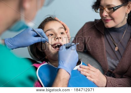 Young Girl With Mother On The First Dental Visit. Senior Male Dentist Doing First Check-up For Patie