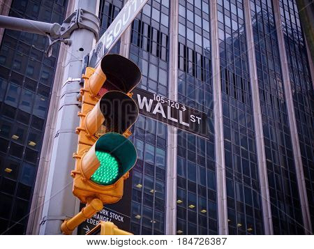View on wall street yellow traffic light with black and white pointer guide. Green traffic light to Wall street banks money dollars finance offices. New York holidays vacations tours and architecture
