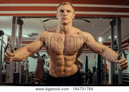 A man with a naked torso doing muscles in the gym