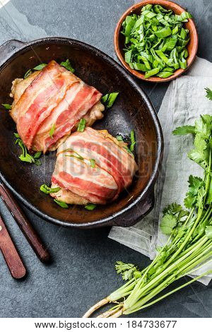 Baked bacon wrapped chicken in clay bowl on stone slate black background. Top view