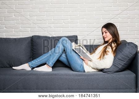 Happy Young Woman Reading Storybook On Couch At Home