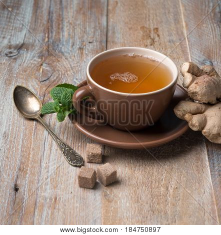 Brown cup of ginger tea with cubes of brown sugar, aged spoon, giner on side