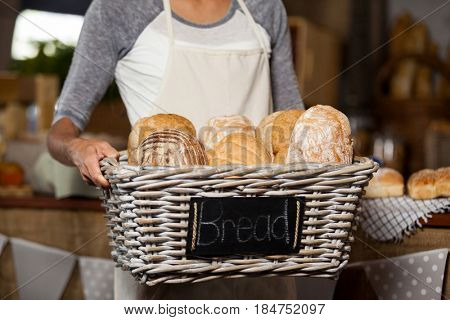 Mid-section of female staff holding wicker basket of various breads at counter in bakery shop