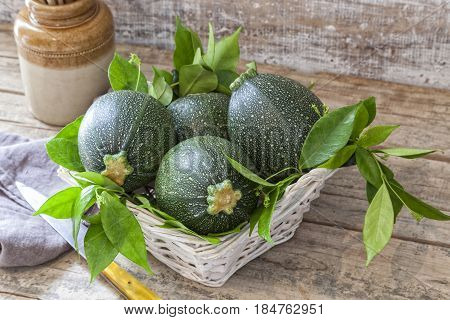 Round zucchini in a basket on a wooden table.
