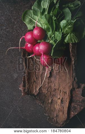 Fresh organic ripe young radish bundle with leaves on wooden bark over dark metal texture background. Top view with space