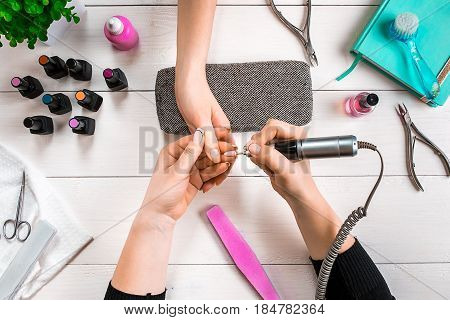 Manicure for the client. Close-up of the hands of a manicurist and client on a wooden background. Nail care. Manicure set and nail polish.