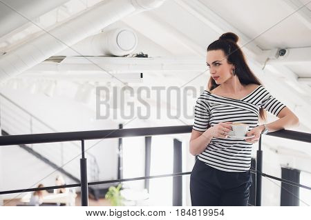 Portrait of woman standing and holding a cup of coffee and cappuccino. Happy adult woman looking away from camera