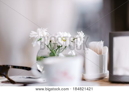 Vase with flowers in a cafe, white daisies, in the background people