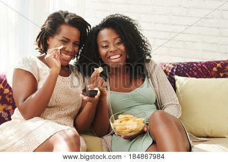 Female friends eating potato chips and watching tv show
