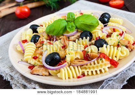 Pasta salad radiatori with chicken black olives blue onion sweet pepper on a dark wooden background.