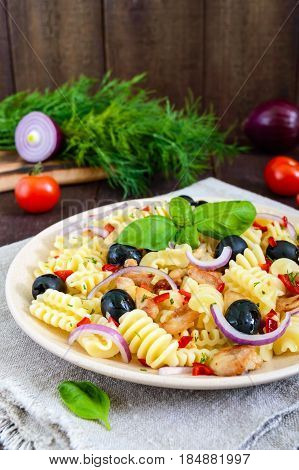 Pasta salad radiatori with chicken black olives blue onion sweet pepper on a dark wooden background. Vertical view.