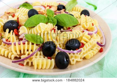 Pasta salad radiatori with chicken black olives blue onion sweet pepper on a white wooden background. Close up