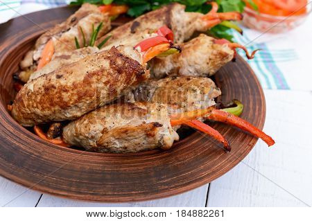 Meat rolls stuffed with sweet pepper carrots in a clay bowl on a white wooden background. Close up