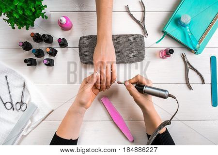 Manicure for the client. Close-up of the hands of a manicurist and client on a wooden background. Nail care. Manicure set and nail polish.