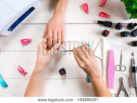 Manicure for the client. Close-up of the hands of a manicurist and client on a wooden background. Nail care. Manicure set and nail polish.