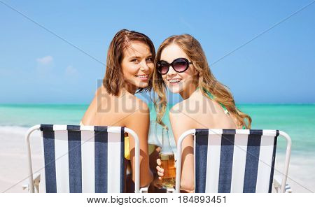summer holidays, vacation, travel and tourism people concept - smiling young women with drinks sunbathing on folding chairs over exotic tropical beach background