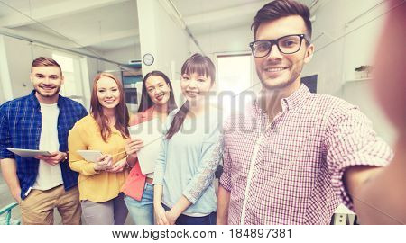 business, technology, startup and people concept - happy international creative business team taking selfie at office