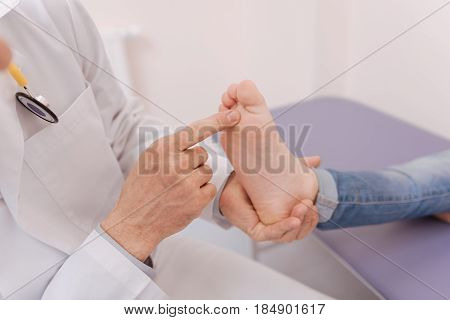 Childs feet. Gentle experienced professional doctor conducting a test for checking patients health while examining her feet