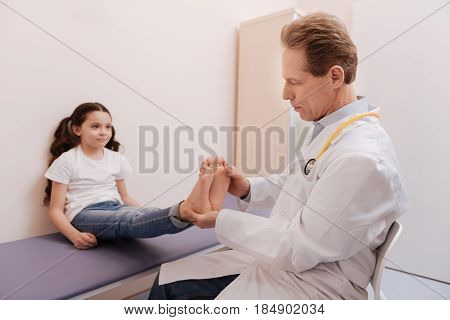Young visitor. Good qualified diligent rheumatologist conducting a checkup and examining patients feet while looking for the cause of the problem