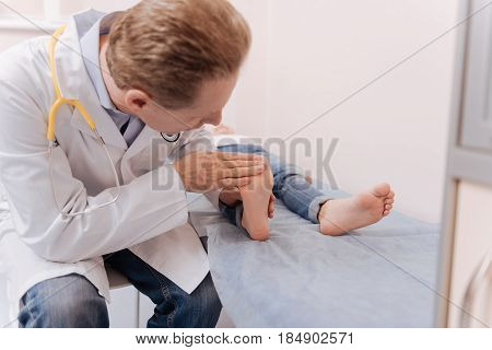 Healing touch. Qualified determined competent rheumatologist treating his patient while she paying him a visit and lying on a bed in his office