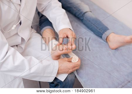 Additional protection. Smart nice diligent rheumatologist applying special elastic bondage for fixating girls joints after conducting a medical procedure