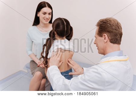 Back posture. Nice competent regular doctor running a checkup on girls spine and looking for a cause of scoliosis