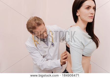 Fixing posture. Scrupulous trained competent doctor consulting his patient and examining her back while working on diagnosis