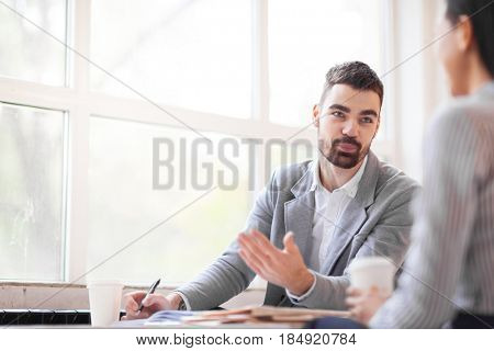 Formal meeting in spacious office: handsome young entrepreneur discussing mutually beneficial conditions with his female business partner, waist-up up portrait