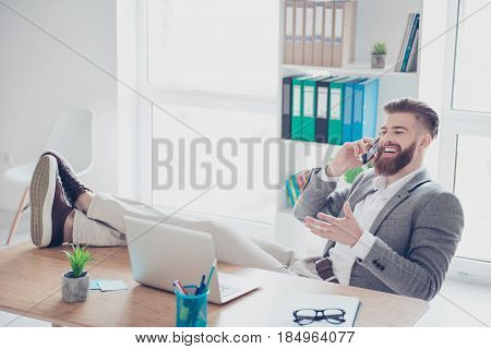 Cheerful Young Successful Man Is Talking On The Phone At The Workplace With Feet On The Table.he Is