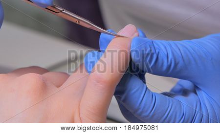 Closeup finger nail care by manicure specialist in beauty salon. Manicurist clear cuticle with professional scissors for manicure