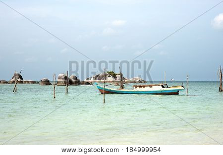 Empty Fishing Boat Docked At The Turquoise Colored Ocean Coast Near White Sand Beach In The Afternoo
