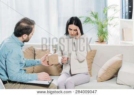 Bearded Psychotherapist With Clipboard Giving Paper Tissues To Upset Young Patient With Glass Of Wat
