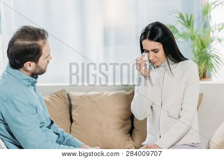 Professional Psychotherapist Looking At Young Female Patient Crying On Couch