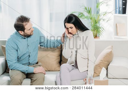 Bearded Psychotherapist Supporting Young Upset Woman Crying On Couch