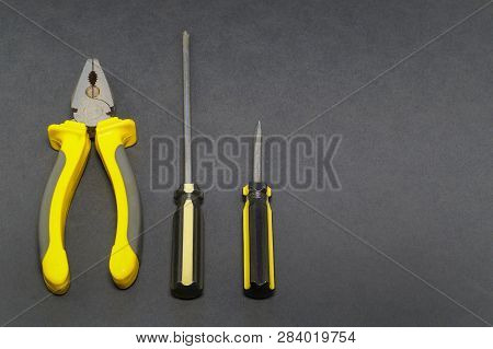 A Set Of Tools On A Gray Background Pliers, Screwdriver, Insulating Tape, Saw.