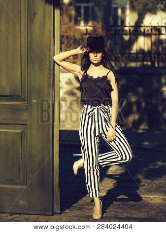Young Beautiful Woman In Stylish Striped Trausers And Black Hat Outdoor Near Green Wooden Door