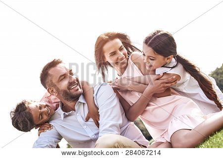 Bonding. Family Of Four Sitting On A Grassy Field Hugging Smilin