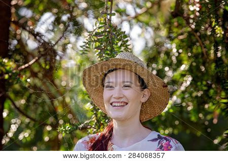 Smiling Happy Young Woman In Straw Hat Standing With A Fine Gossamer Spider Cobweb Amongst The Trees