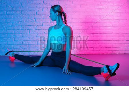 Tender Young Slim Gymnast Woman In Sports Clothing Stretching With Elastic Band In Front Of Brick Wa